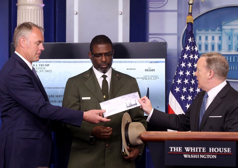 Image: White House press secretary Sean Spicer gives Interior Secretary Ryan Zinke the first quarter check of President Trump's salary, which he donated to the National Park Service, as Tyrone Brandyburg looks on.