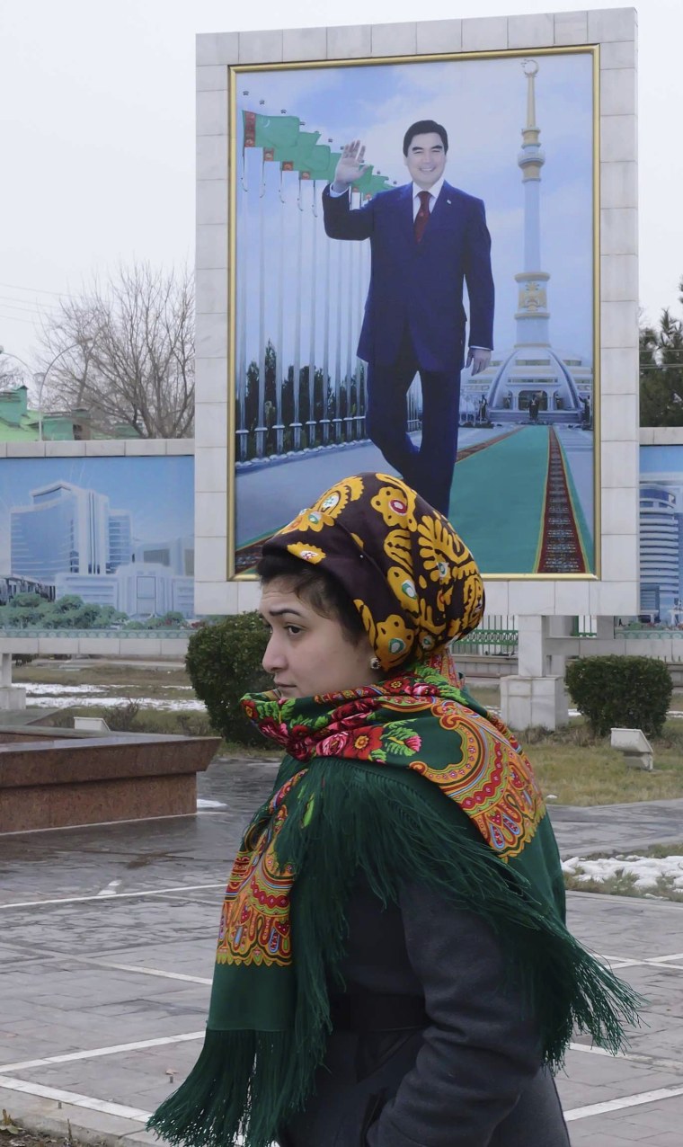 Image: A woman walks past a board displaying a portrait of Turkmenistan's President Berdimuhamedov in Ashgabat