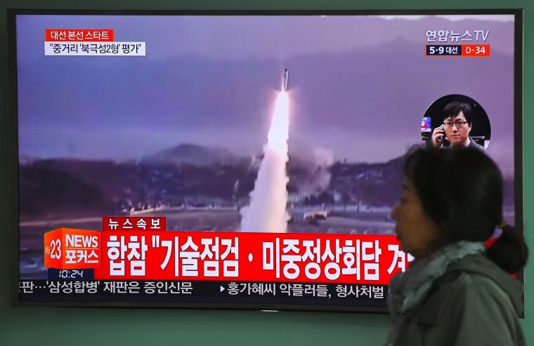 Image: A woman walks past a television screen showing file footage of a North Korean missile launch