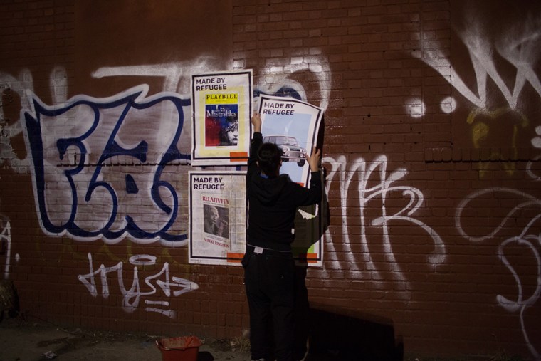 Kien Quan installing a mural in Bushwick, Brooklyn, with large Made by Refugee posters.