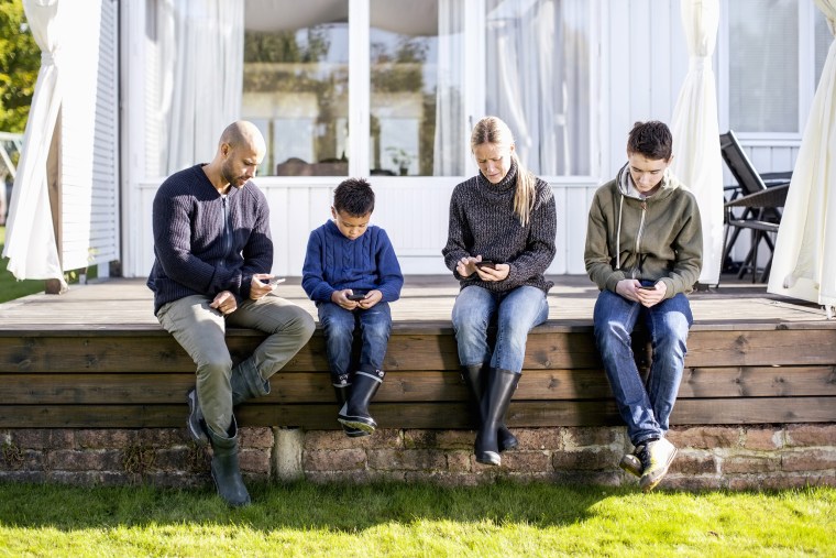Family of four using mobile phones at yard