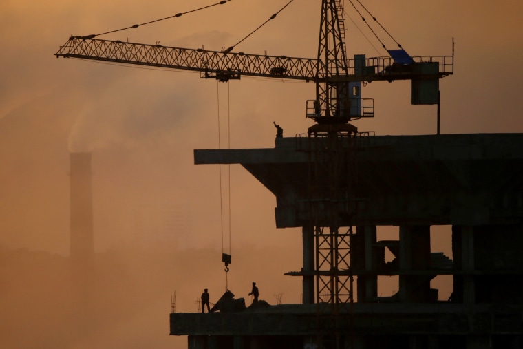 Image: People work atop a building under construction as sun sets in Pyongyang