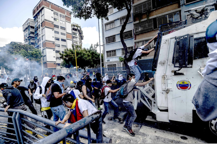 Image: Protestors try to climb onto a water cannon vehicle during protests in Venezuela