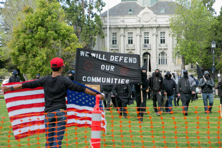Image: A Trump supporter holds an American flag while an anti-fascist group marches into the park  during a free speech rally at Martin Luther King Jr. Civic Center Park in Berkeley, California, April 15.