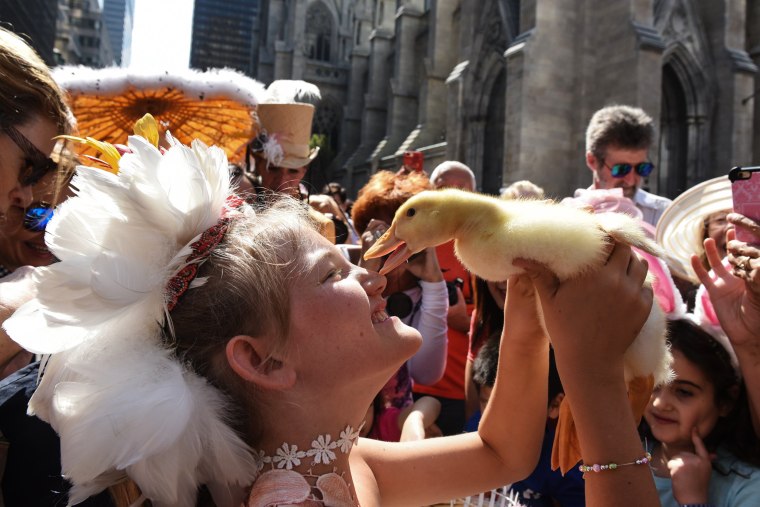 Image: A girl holds a duck while wearing a fanciful hat during the Easter Parade