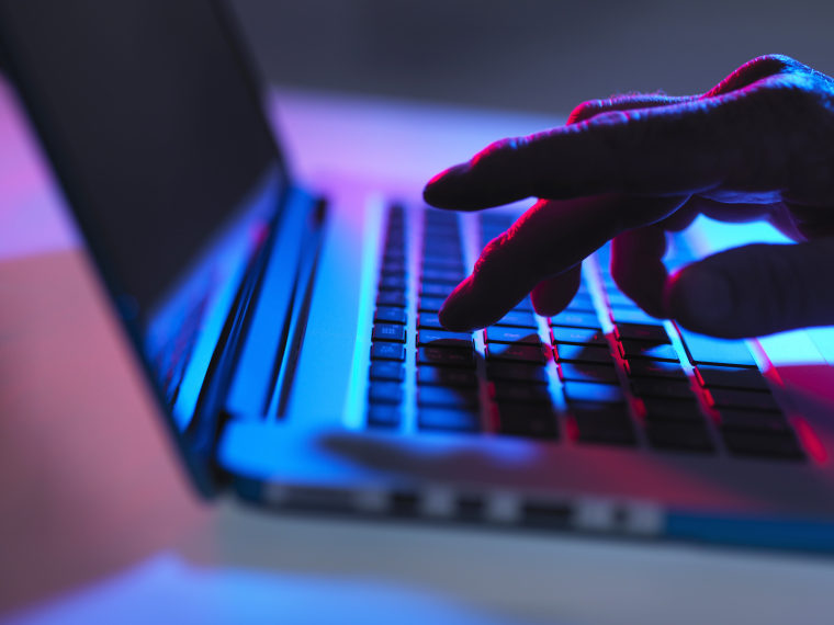 Image: Silhouette of male hand typing on laptop keyboard at night