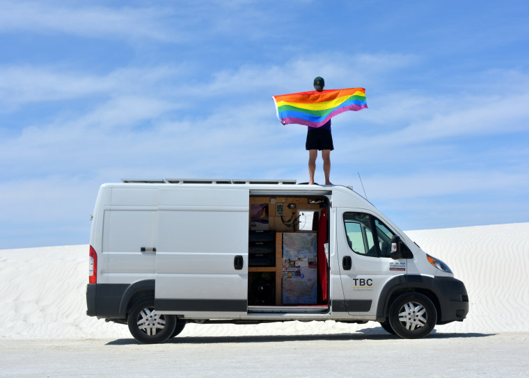 Mikah Meyer standing on top of his van with rainbow flag at White Sand National Monument in New Mexico