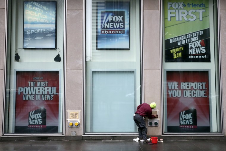 Image: A worker cleans a sign outside the Fox television studios