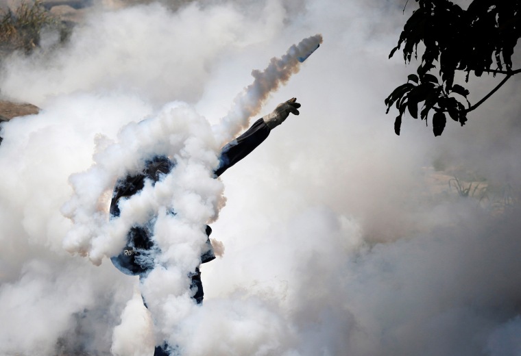Image: A demonstrator throws back a tear gas grenade while clashing with riot police in Caracas