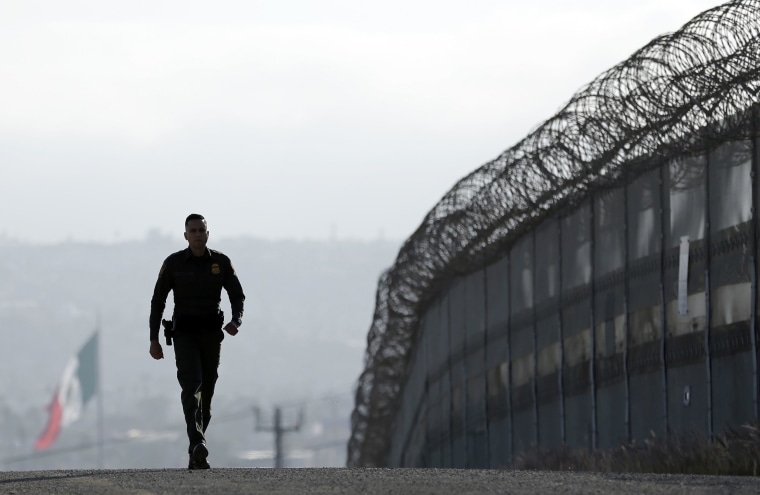 Image: A Border Patrol agent walks near a fence in San Diego