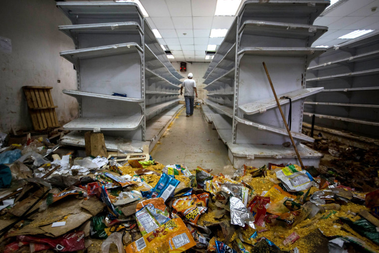 Image: A man walks down the aisle of a destroyed grocery store 