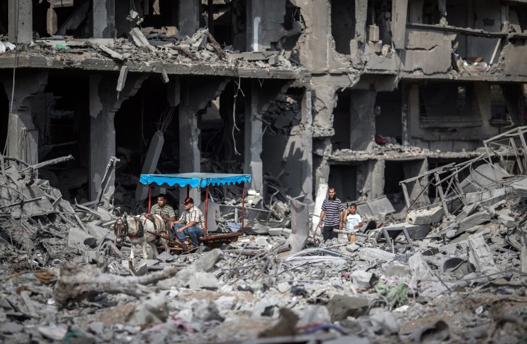 Image: Palestinians on a horse cart drive past destroyed buildings on their way to their homes in Beit Hanoun, northern Gaza Strip