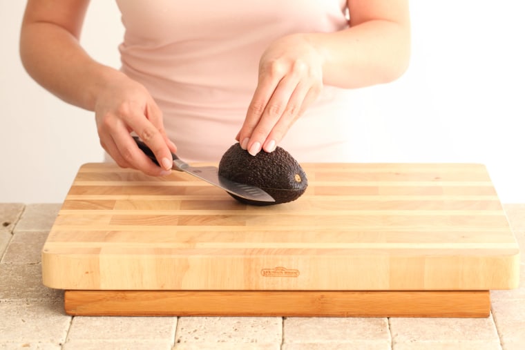 Young man cutting avocado top view on wooden cutting board. Perfectly ripe  avocado in hands, making toasts in modern white kitchen. Healthy eating and  Home cooking concept. photo – Food Image on