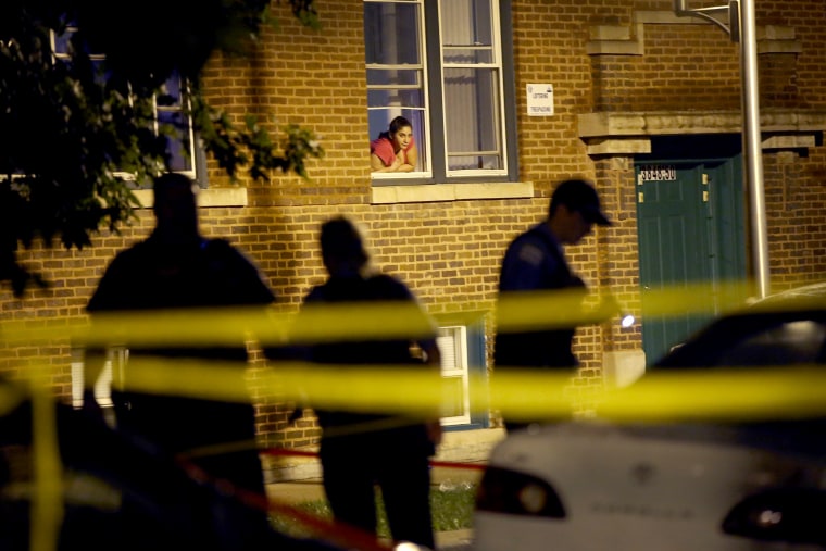 Image: A woman watches from her window as police look for evidence after 20-year-old Carlos Barron was shot and killed in the Humboldt Park neighborhood on July 19, 2013 in Chicago, Illinois.