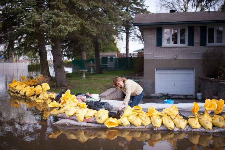 Image: A resident of the Montreal borough of Pierrefonds, uses a pool pump to protect her home from flood waters