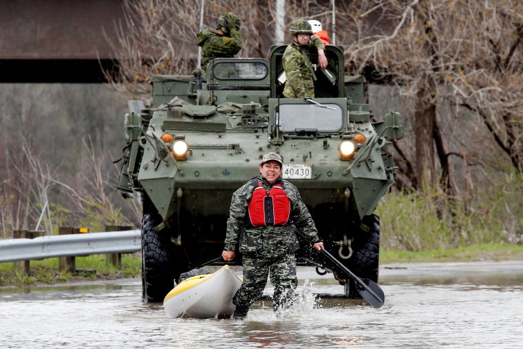 Image: A woman pulls a kayak in front of Canadian soldiers in a flooded residential area in Gatineau