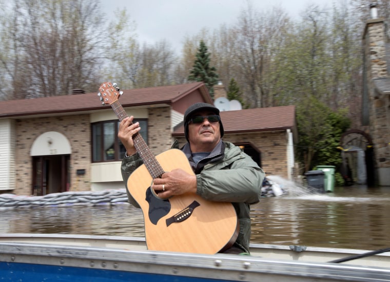 Image: A man plays his guitar as he travels in a boat to collect water supplies in a flooded residential neighbourhood in Ile Bizard