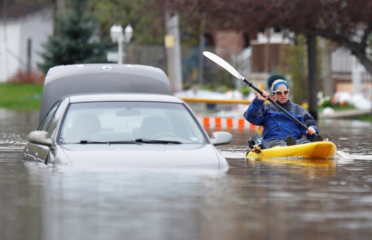 Image: A woman paddles a kayak past an abandoned car on a flooded residential street in Gatineau