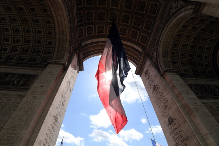 Image: A giant French flag hang fro the Arc de Triomphe in honour of President Emmanuel Macron attends a ceremony at the Tomb of the Unknown Soldier in Paris