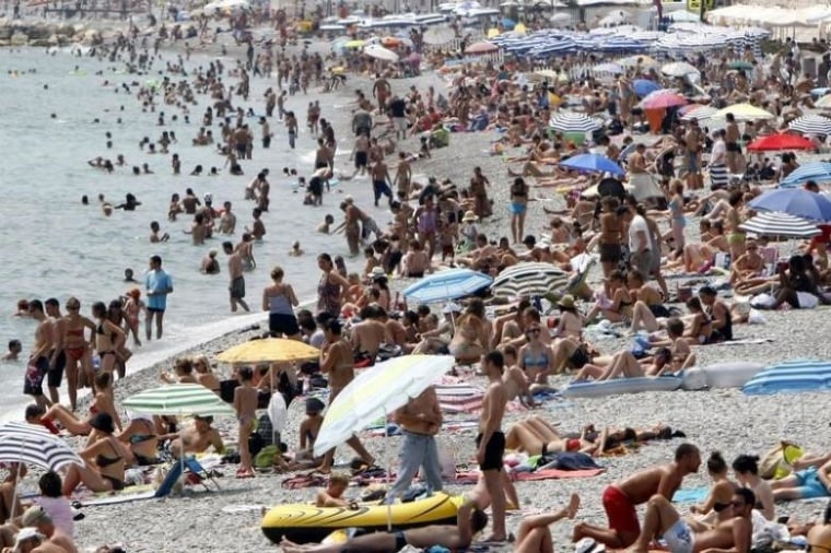 Holidaymakers and tourists sunbathe on the beach on a hot summer day in Nice