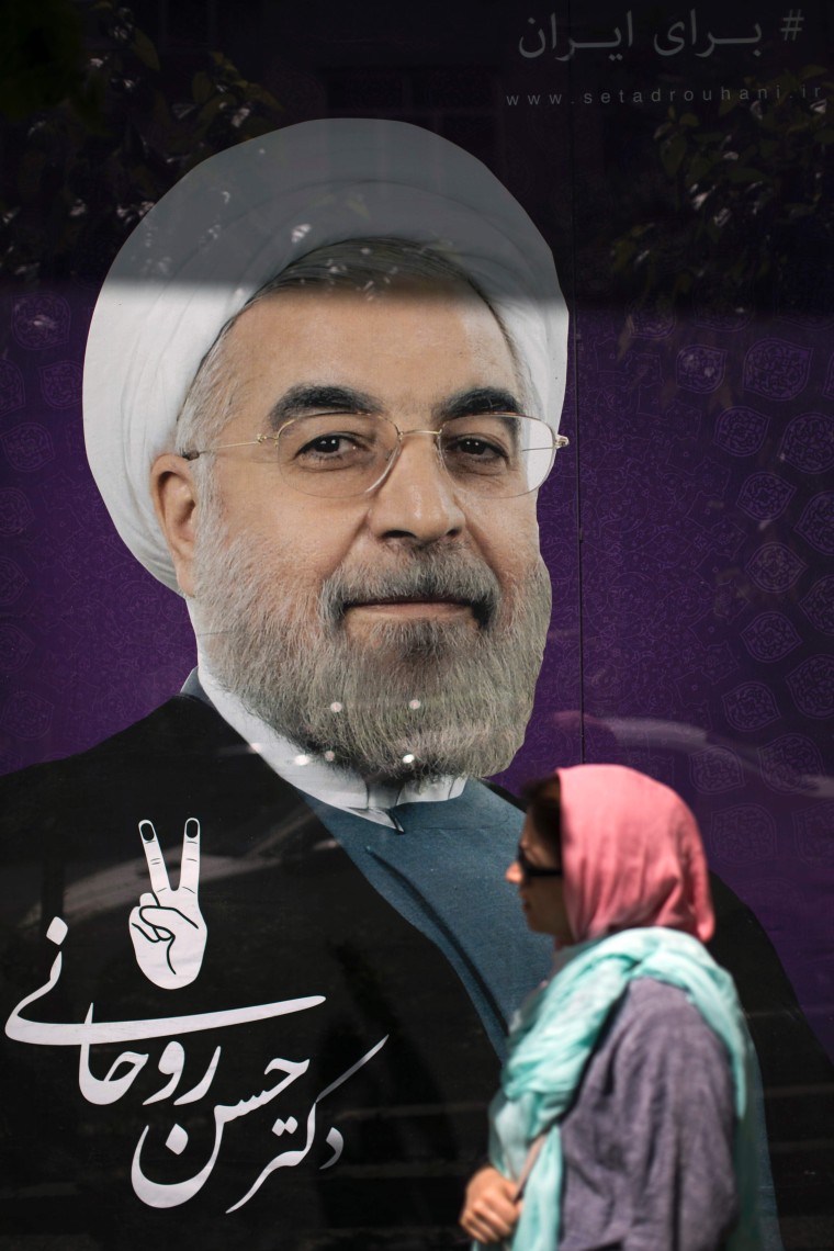 Image: An Iranian woman walks past portraits of President Hassan Rouhani