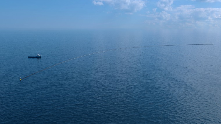 A computer rendering shows the Ocean Cleanup system with a support vessel.