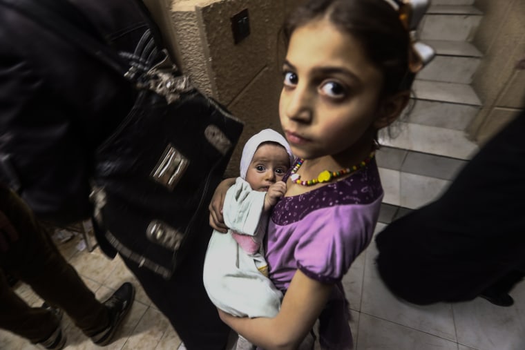 Image: A little girl holding her newborn sister waits for their turn for vaccinations