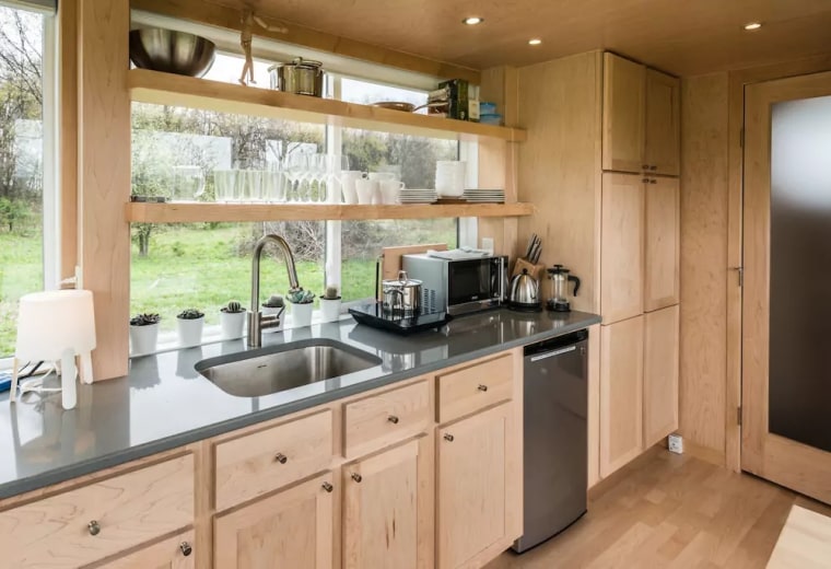 The full kitchen includes an induction cooktop, mini-fridge, sink, electric kettle, microwave, French press and plenty of shelving for dishware.