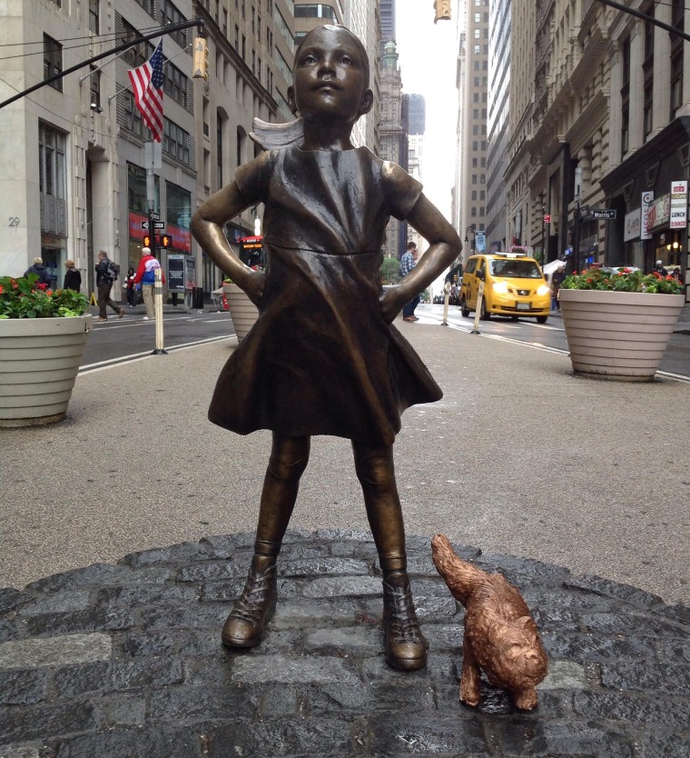 Artist Alex Gardega places his "sketchy dog" statue next to "Fealess Girl."
