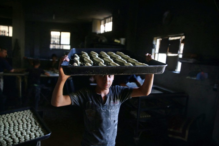 Image: A boy carries raw pastries prior to baking, to be sold during Ramadan in the rebel held besieged eastern Damascus suburb of Ghouta