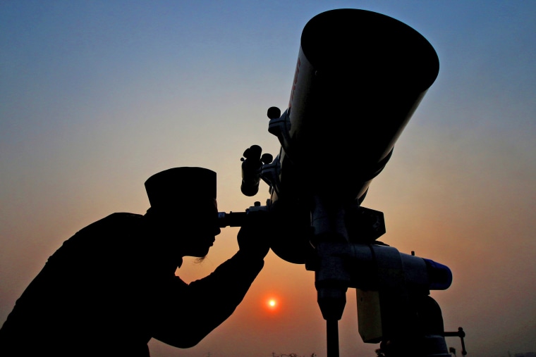 Image: An official looks through a telescope for the sighting of the new moon for the start of the Muslim fasting month of Ramadan at a religious boarding school in Jakarta