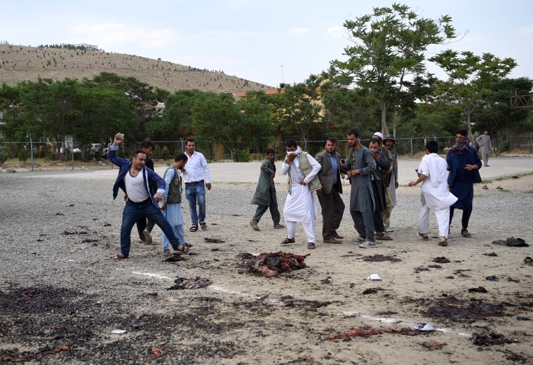 Image: An angry Afghan man throws a rock at what was thought to be the remains of one of the attackers.