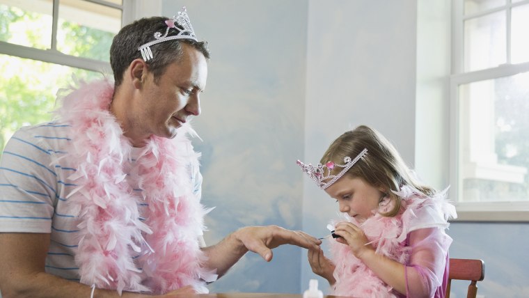 Little girl painting fathers fingernails at table