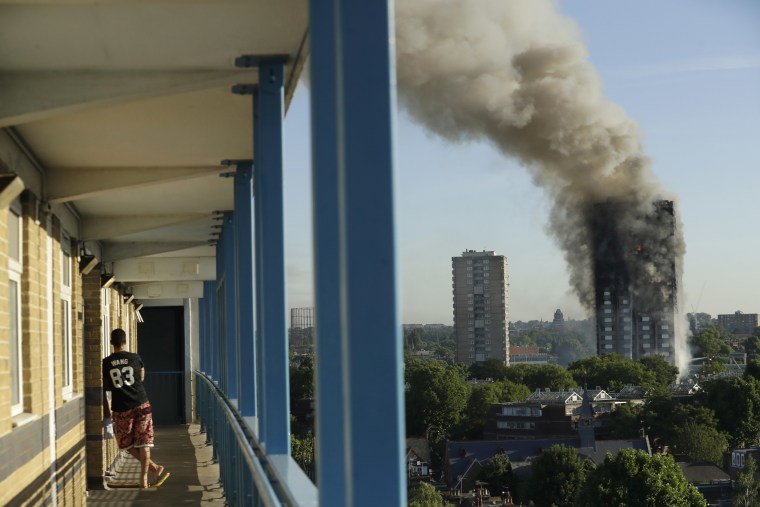 Image: A resident in a nearby building watches smoke rise from a building on fire in London