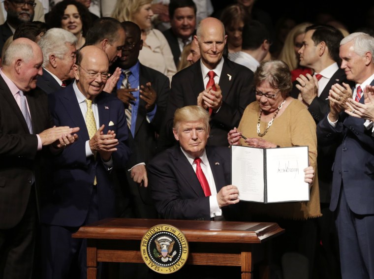 Image: President Donald Trump shows an signed executive order surrounded by cabinet members and supporters in Miami