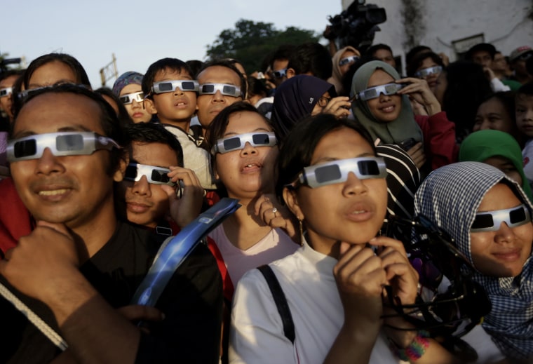 Image: People look up at the sun wearing protective glasses to watch a solar eclipse