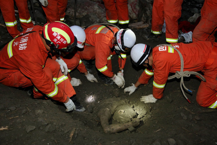 Image: Rescue workers try to remove the body of a victim at the site of a landslide