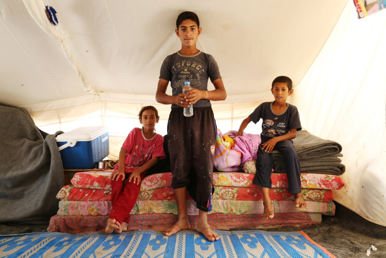 Image: Atallah Saleh, 15, stands inside a tent with his siblings at the Hammam al-Alil refugee camp in northern Iraq