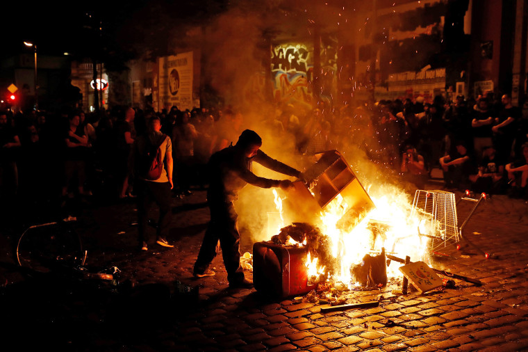 Image: A man throws a shelf on to burning pile of bins after the \"Welcome to Hell\" rally