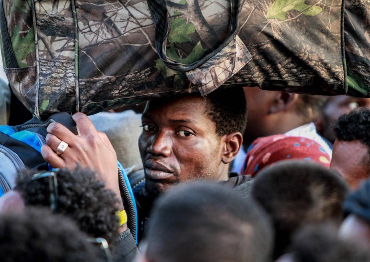 Image: A man carries his belongings on his head during the evacuation of a makeshift camp