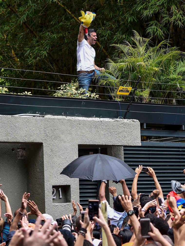 Image: Venezuelan opposition leader Leopoldo Lopez displays the Venezuelan national flag as he greets supporters gathering outside his house