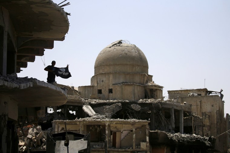 Image: A member of Iraqi security forces holds a flag of Islamic State militants on the top of a destroyed building from clashes in the Old City of Mosul