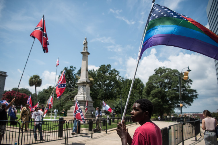 Image: Nathaniel Simmons holds a rainbow colored American flag as demonstrators fly Confederate flags