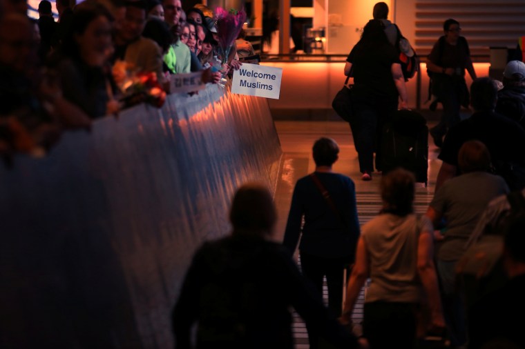 Image: Retired engineer John Wider, 59, holds up a sign reading "Welcome Muslims" as international travelers arrive at Los Angeles International Airport