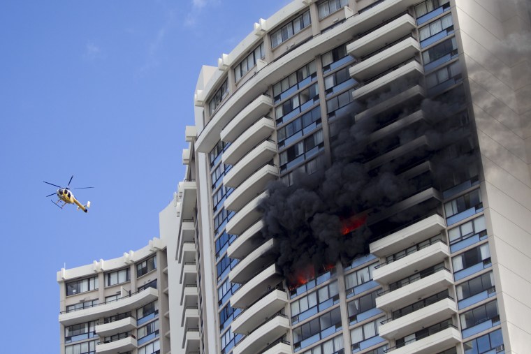Image: A Honolulu Fire Department helicopter flies near a fire burning on a floor at the Marco Polo apartment complex