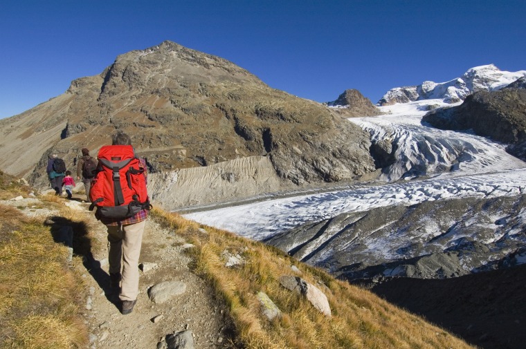 Hikers on a path with Vadret Pers, a side glacier and main Morteratsch glacier in background.