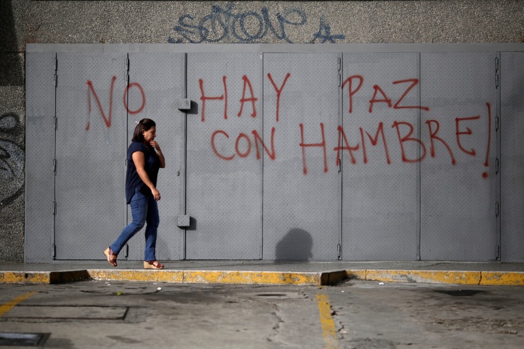 Image: A woman walks in front of a graffiti that reads "There is no peace with hunger" during a strike called to protest against Venezuelan President Nicolas Maduro's government in Caracas