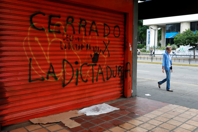 Image: A woman walks on a street close to a graffiti that reads \"closed because of the dictatorship\" during a national strike in Venezuela.