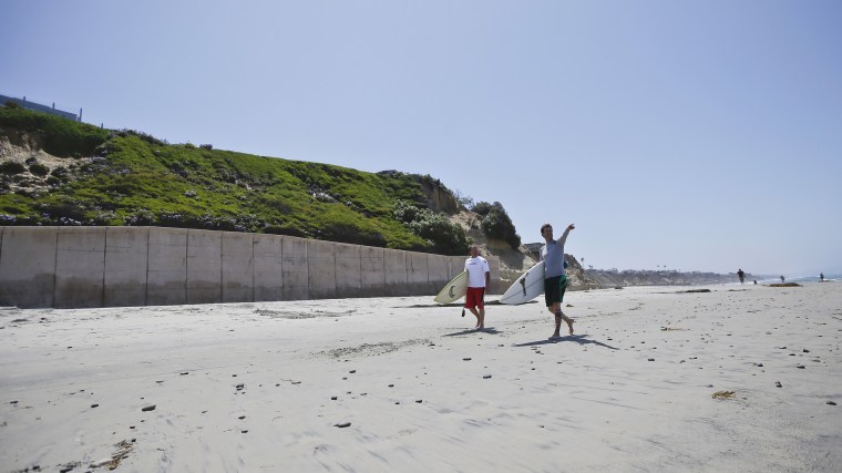 Surfers walk the sand in Solana Beach, Calif., in 2013, below a seawall which holds back the ocean and supports the hill side where homes sit precariously perched atop cliffs.