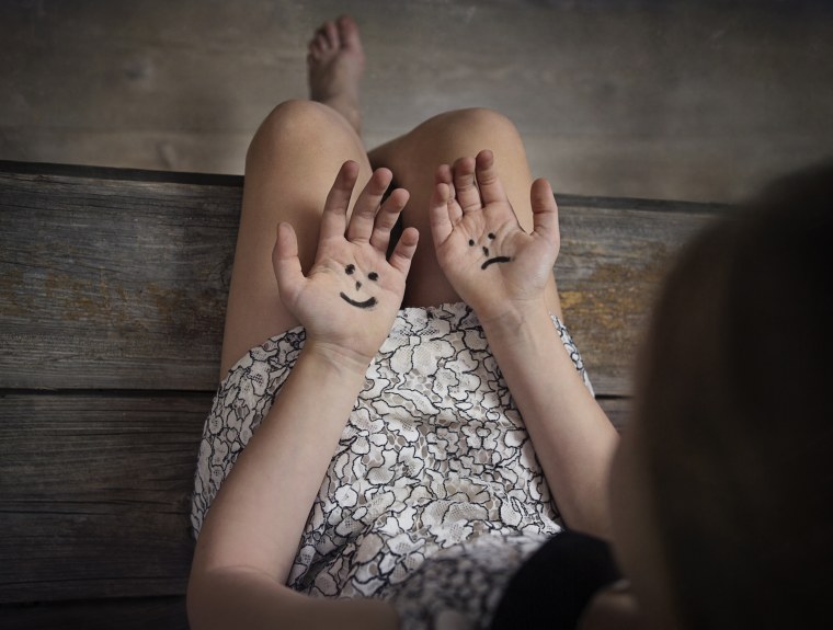 Image: A young girl looks at conflicting emotions on her hands.